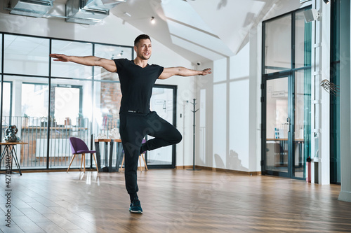 Sportive man standing in yoga pose with spread arms