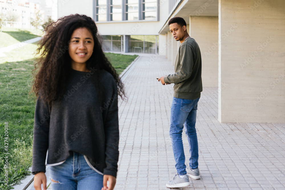 Afro Latino man with mobile phone looks amazed and in love with a curly-haired African American girl walking down the street happy and cheerful. Horizontal photography and copy space Afro Latino man with mobile phone looks amazed and in love with a curly-haired African American girl walking down the street happy and cheerful. Horizontal photography and copy space