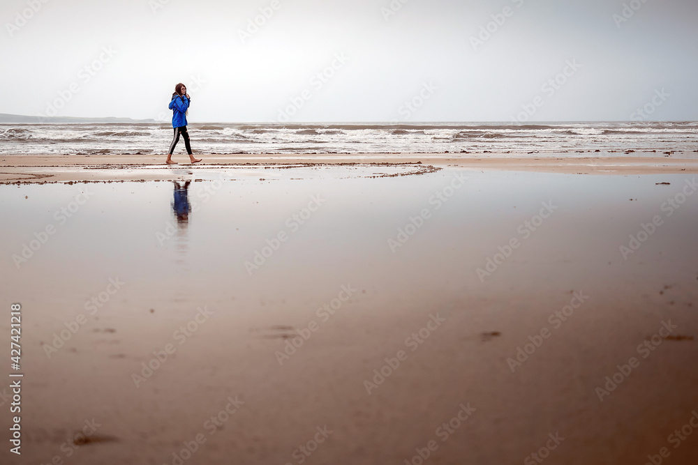 Teenager girl walking on a sandy beach. The model dressed in blue jacket and black leggins. Outdoor activity concept. Selective focus. Warm tone Teenager girl walking on a sandy beach. The model dressed in blue jacket and black leggins. Outdoor activity concept. Selective focus. Warm tone