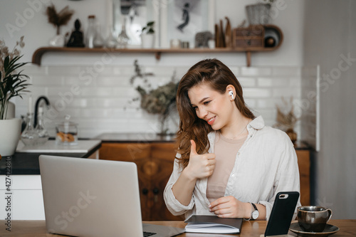 Smiling young pretty woman office worker business lady listening to an online webinar on laptop, taking notes in notebook, working on freelance project at home, remote work, learning at home concept © Oleksandr