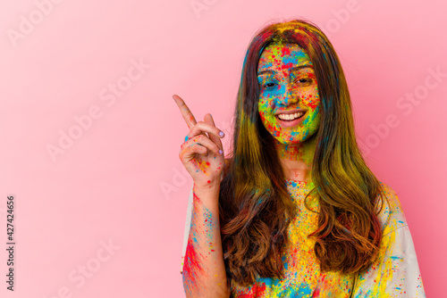 Young Indian woman celebrating holy festival isolated on white background smiling cheerfully pointing with forefinger away.