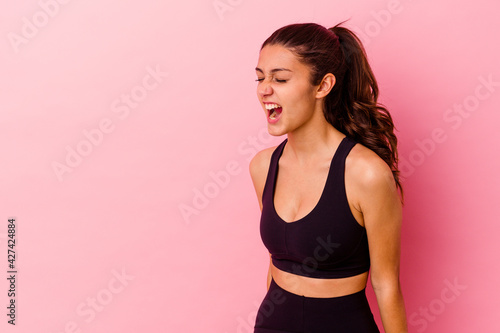 Young sport Indian woman isolated on pink background shouting towards a copy space © Asier