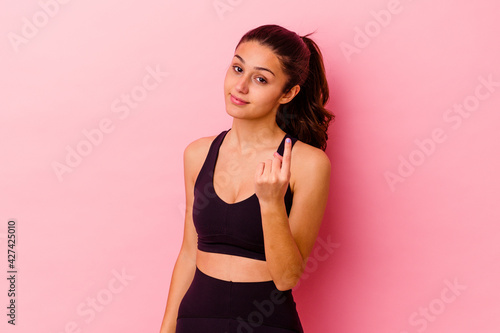 Young sport Indian woman isolated on pink background pointing with finger at you as if inviting come closer.