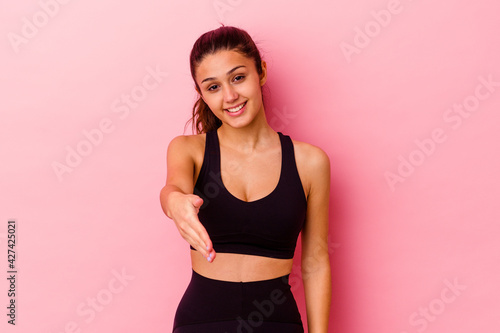 Young sport Indian woman isolated on pink background stretching hand at camera in greeting gesture.