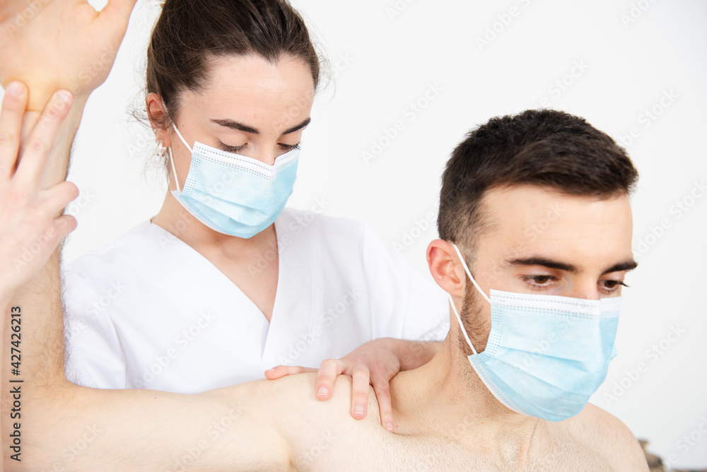 Closeup view of a physiotherapist treating a patient while wearing a face mask during Coronavirus pandemic.