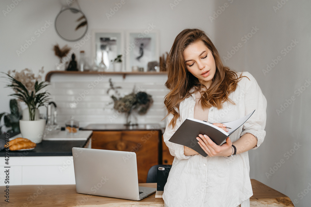 portrait of young woman in comfortable clothes with notepad, planning work and expenses at home