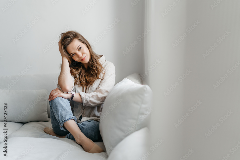 Нoung woman is sitting on the sofa in the living room. A beautiful blonde in white comfortable home clothes. Нoung woman is sitting on the sofa in the living room. A beautiful blonde in white comfortable home clothes.