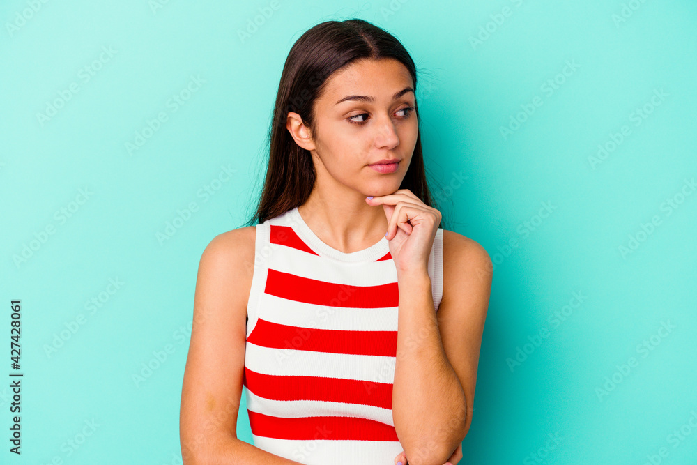 Young Indian woman isolated on blue background thinking and looking up, being reflective, contemplating, having a fantasy.