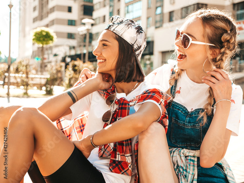 Two young smiling beautiful female with colorful penny skateboards. Women in summer hipster clothes sitting in the street background. Positive models having fun and going crazy