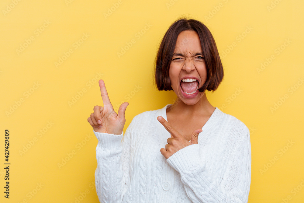 Young mixed race woman isolated on yellow background pointing with forefingers to a copy space, expressing excitement and desire. Young mixed race woman isolated on yellow background pointing with forefingers to a copy space, expressing excitement and desire.