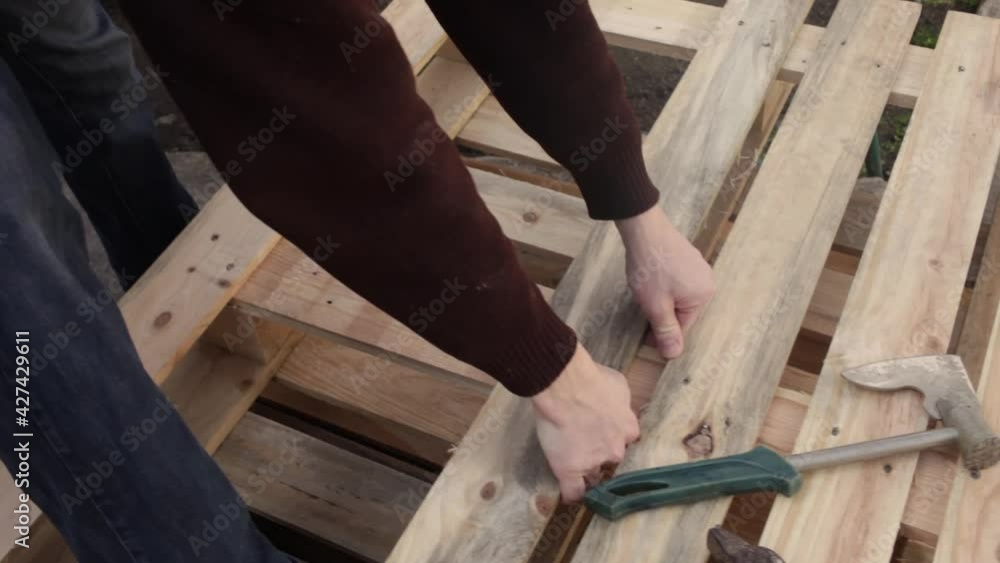 A young man disassembles a pallet. A wooden pallet, garden furniture. A man rips off the boards to make a table. Cheap DIY master eco-friendly wasteless with their own hands top view A young man disassembles a pallet. A wooden pallet, garden furniture. A man rips off the boards to make a table. Cheap DIY master eco-friendly wasteless with their own hands top view