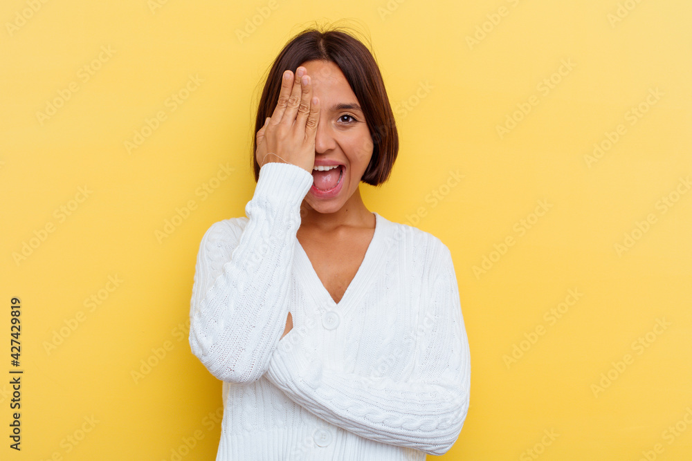 Young mixed race woman isolated on yellow background having fun covering half of face with palm. Young mixed race woman isolated on yellow background having fun covering half of face with palm.