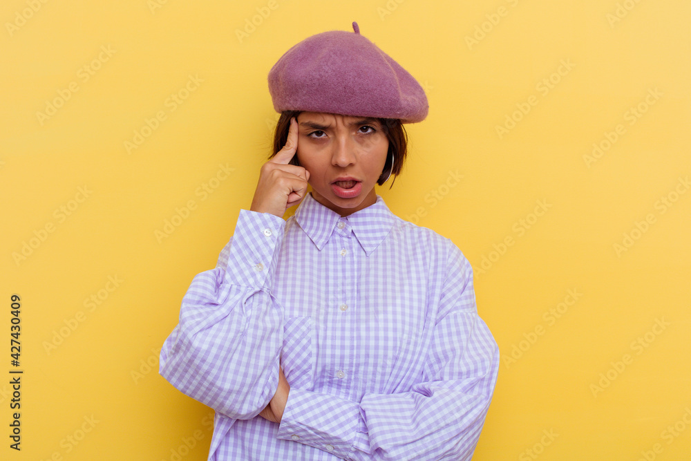 Young mixed race woman wearing a beret isolated on yellow background pointing temple with finger, thinking, focused on a task. Young mixed race woman wearing a beret isolated on yellow background pointing temple with finger, thinking, focused on a task.