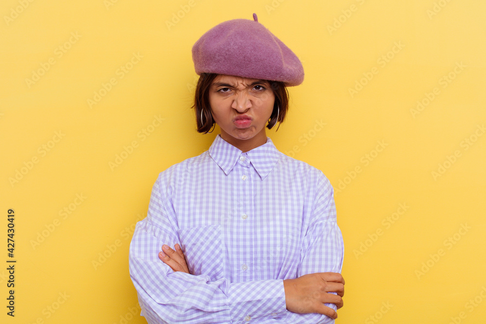 Young mixed race woman wearing a beret isolated on yellow background frowning face in displeasure, keeps arms folded. Young mixed race woman wearing a beret isolated on yellow background frowning face in displeasure, keeps arms folded.