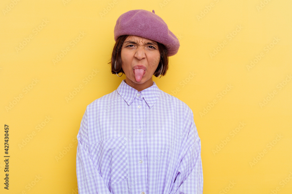 Young mixed race woman wearing a beret isolated on yellow background funny and friendly sticking out tongue. Young mixed race woman wearing a beret isolated on yellow background funny and friendly sticking out tongue.