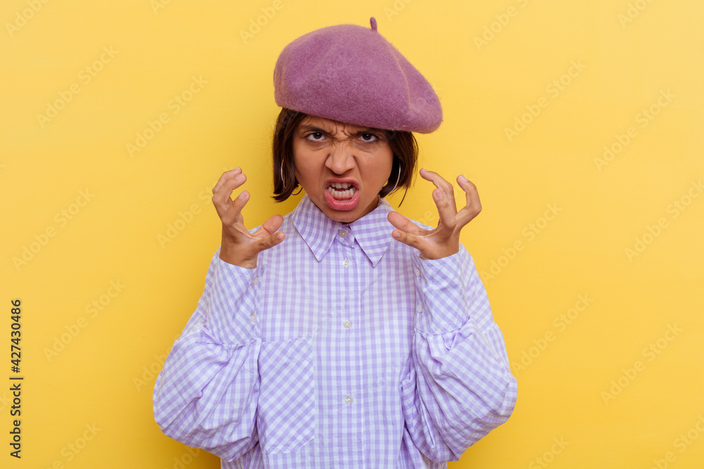 Young mixed race woman wearing a beret isolated on yellow background upset screaming with tense hands. Young mixed race woman wearing a beret isolated on yellow background upset screaming with tense hands.