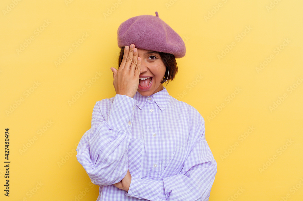 Young mixed race woman wearing a beret isolated on yellow background having fun covering half of face with palm. Young mixed race woman wearing a beret isolated on yellow background having fun covering half of face with palm.