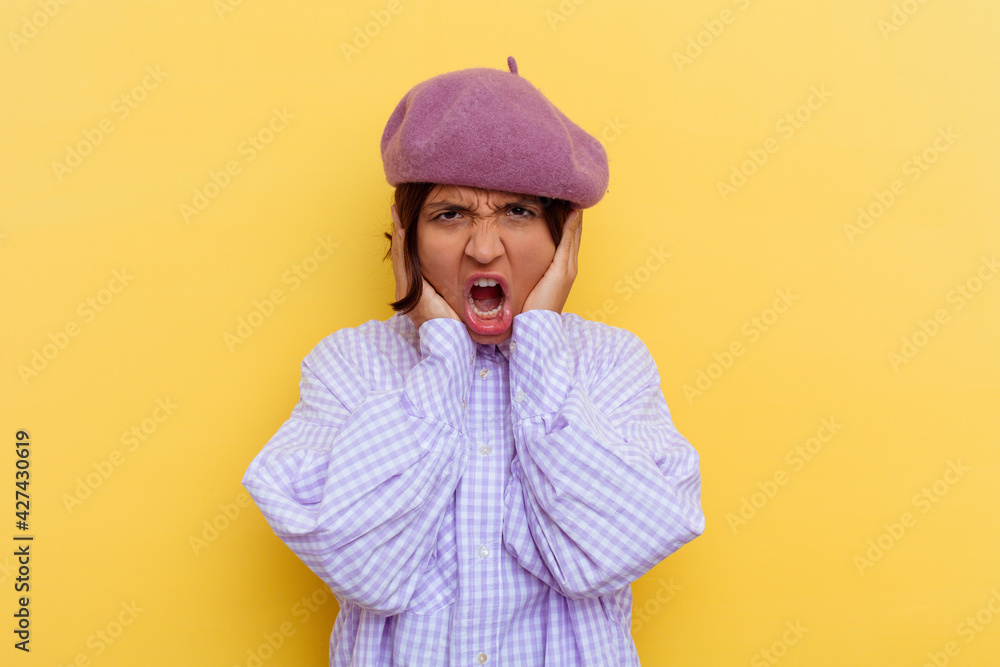 Young mixed race woman wearing a beret isolated on yellow background covering ears with hands trying not to hear too loud sound. Young mixed race woman wearing a beret isolated on yellow background covering ears with hands trying not to hear too loud sound.