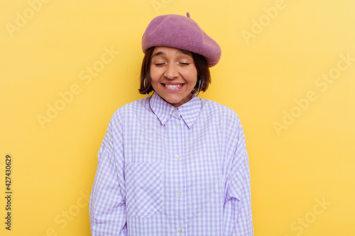 Young mixed race woman wearing a beret isolated on yellow background laughs and closes eyes, feels relaxed and happy.