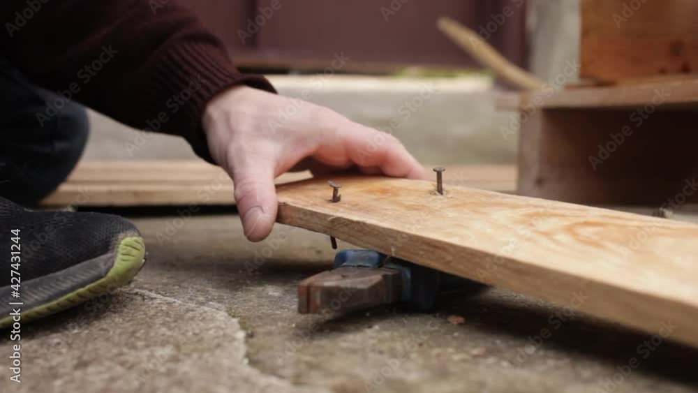 A young man pulls nails out of a wooden board. Pallet. Tick tool asphalt A young man pulls nails out of a wooden board. Pallet. Tick tool asphalt