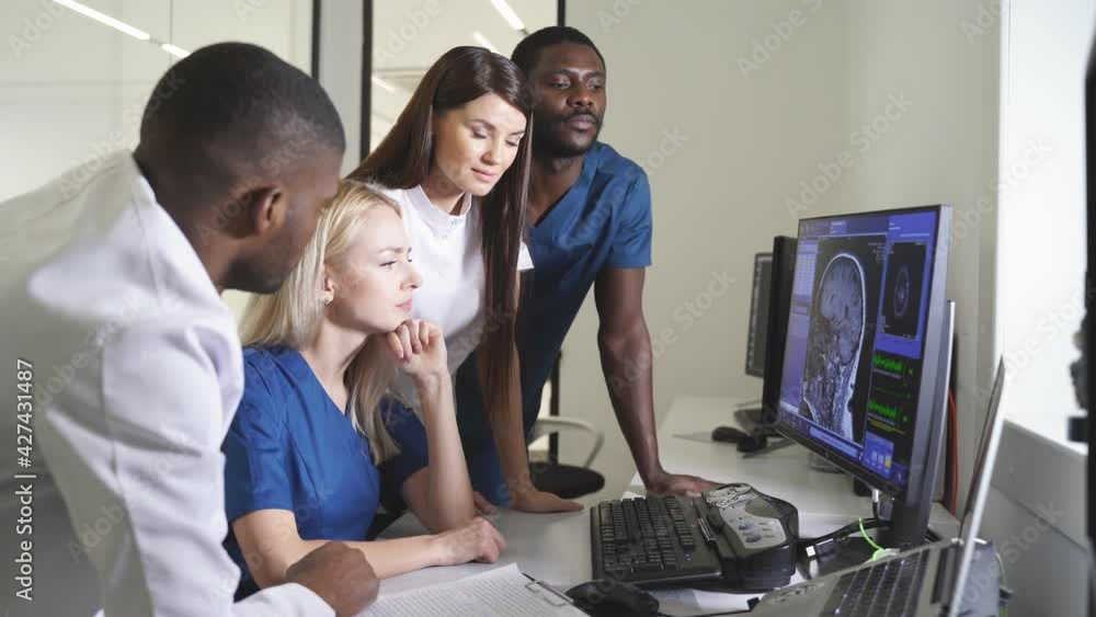 Interracial radiologists sitting at table in front of computer monitors and discussing diagnosis in team at office. Medicine concept. Interracial radiologists sitting at table in front of computer monitors and discussing diagnosis in team at office. Medicine concept.