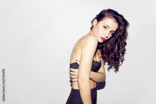 Front view of an attractive brunette young woman in black lengerie is possing and looking at camera on grey background.