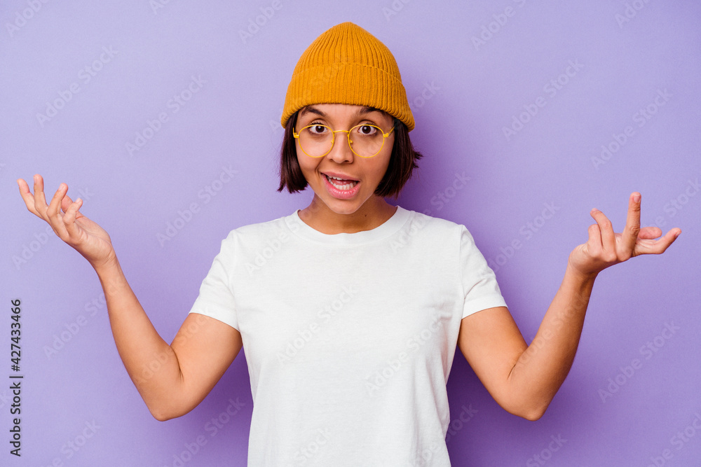 Young mixed race woman wearing a wool cap isolated on purple background receiving a pleasant surprise, excited and raising hands.