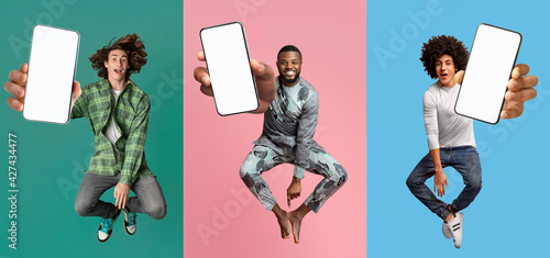Cool young guys with empty smartphones jumping up in air over colorful studio backgrounds, mobile application mockup photo