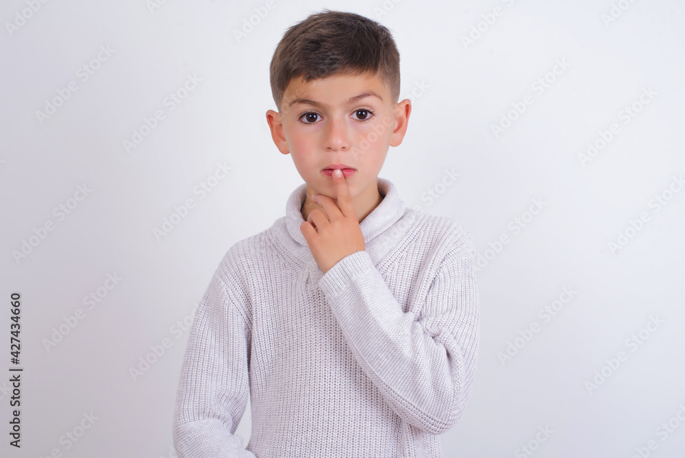 Nervous puzzled Caucasian kid boy wearing knitted sweater against white wall opens mouth from surprise, reacts on sudden news. Nervous puzzled Caucasian kid boy wearing knitted sweater against white wall opens mouth from surprise, reacts on sudden news.