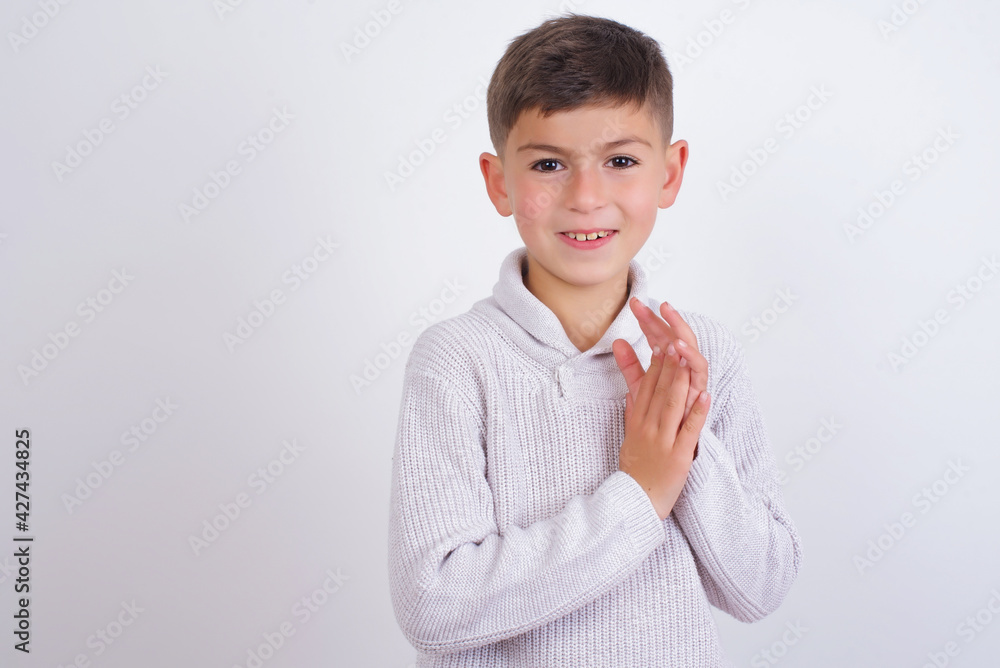 Caucasian kid boy wearing knitted sweater against white wall clapping and applauding happy and joyful, smiling proud hands together. Caucasian kid boy wearing knitted sweater against white wall clapping and applauding happy and joyful, smiling proud hands together.