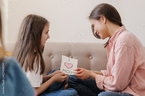 A dark-haired girl congratulates her mother on Mother's Day, gives her a homemade greeting card.Home interior design.The concept of Mom's Day,March 8 and Birthday.