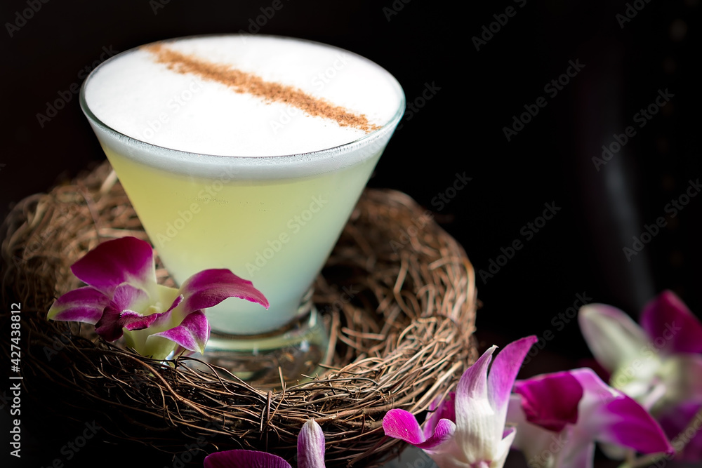 Close up on a sophisticated sour cocktail made with gin, egg white, lemon, and sugar, served in a small nest decorated with orchid flowers. Presentation made for Easter Close up on a sophisticated sour cocktail made with gin, egg white, lemon, and sugar, served in a small nest decorated with orchid flowers. Presentation made for Easter