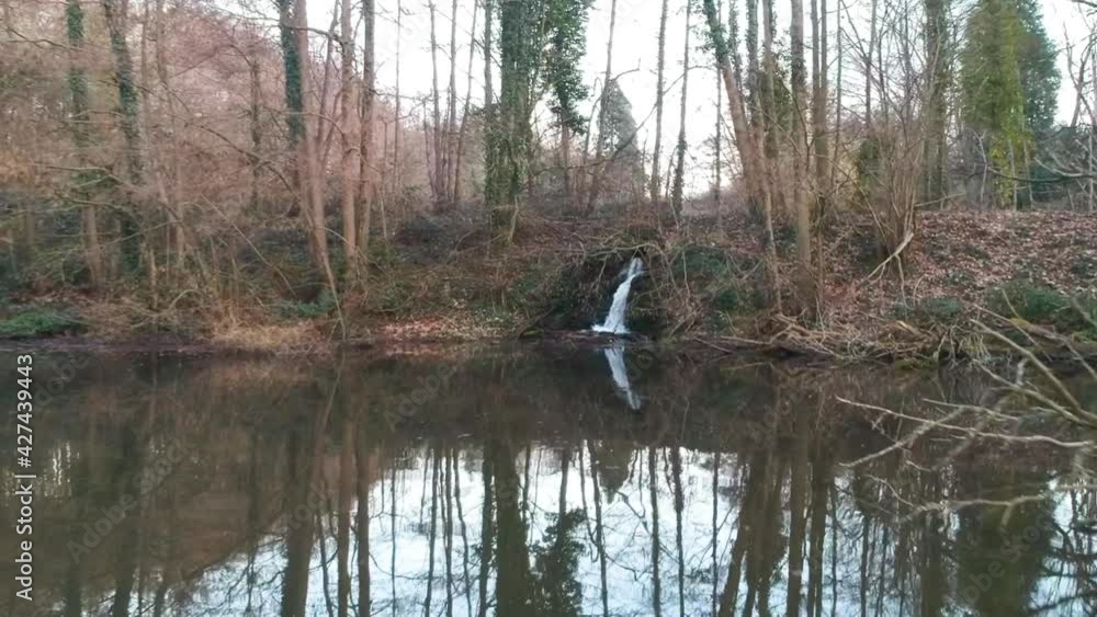 Push in aerial drone drainpipe water streaming into pond cloudy day