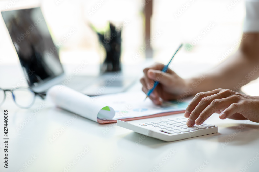 Close up Business man using calculator and laptop for do math finance on wooden desk, tax, accounting, statistics and analytical research concept Close up Business man using calculator and laptop for do math finance on wooden desk, tax, accounting, statistics and analytical research concept