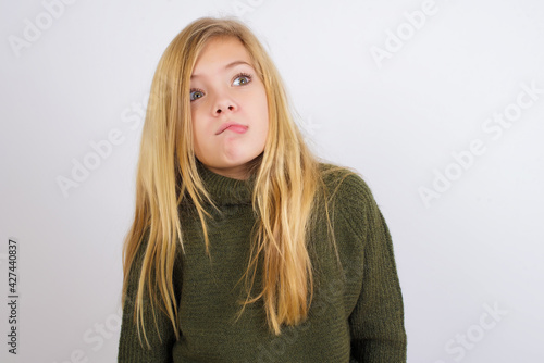 Caucasian kid girl wearing green knitted sweater against white wall making grimace and crazy face, screaming out of control, funny lunatic expressing freedom and wild.