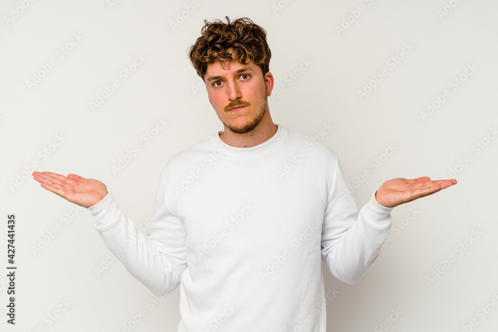 Young caucasian man isolated on white background confused and doubtful shrugging shoulders to hold a copy space. Young caucasian man isolated on white background confused and doubtful shrugging shoulders to hold a copy space.