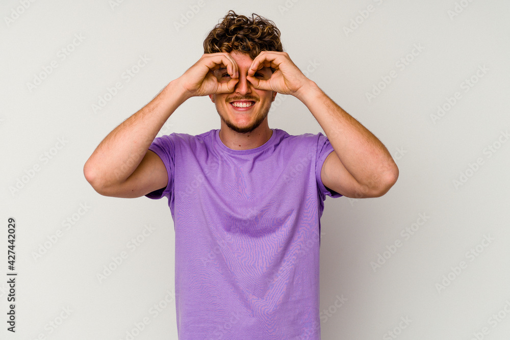 Young caucasian man isolated on white background showing okay sign over eyes Young caucasian man isolated on white background showing okay sign over eyes