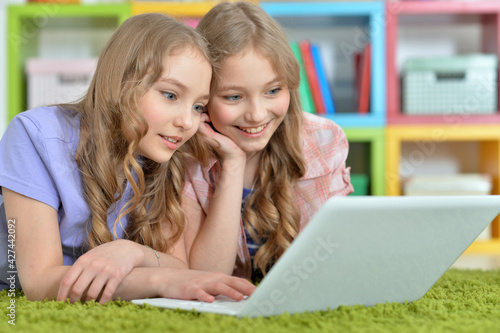 Two pretty little girls lying on floor and using laptop