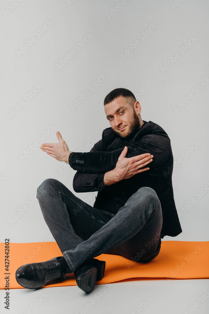 A businessman in a black suit doing yoga on an orange rug. Sports and business. A businessman in a black suit doing yoga on an orange rug. Sports and business.