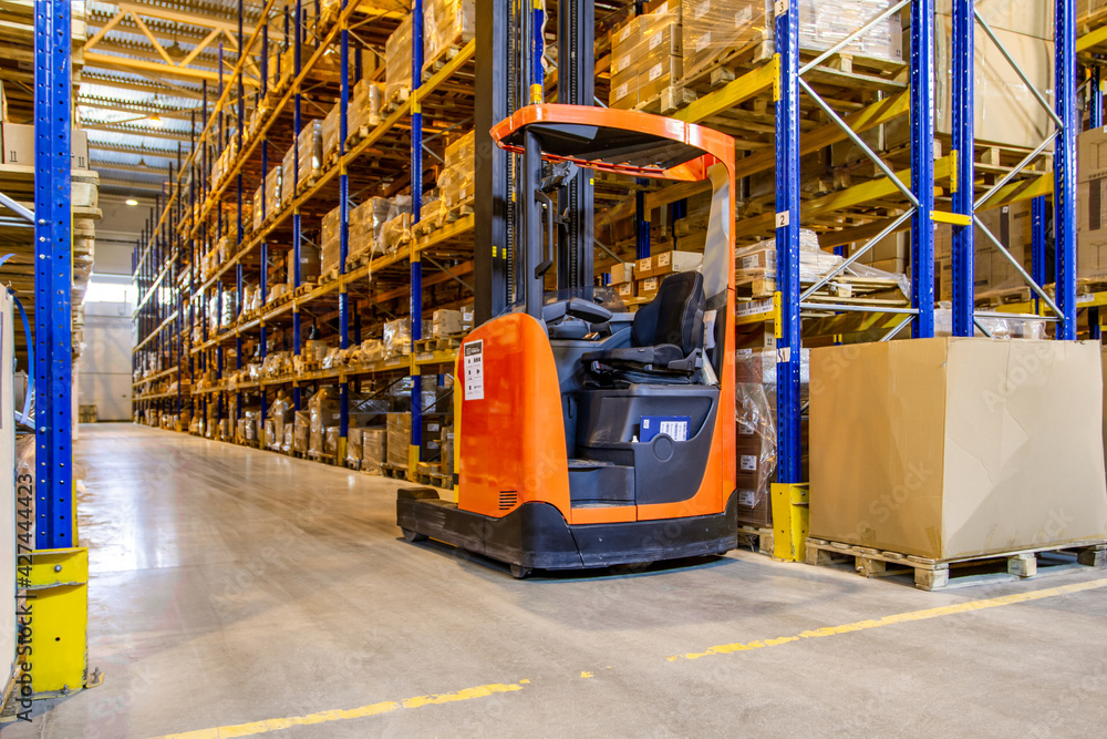 Interior of a modern warehouse storage with rows and goods boxes on high shelves. Pallet truck parking near shelves Interior of a modern warehouse storage with rows and goods boxes on high shelves. Pallet truck parking near shelves