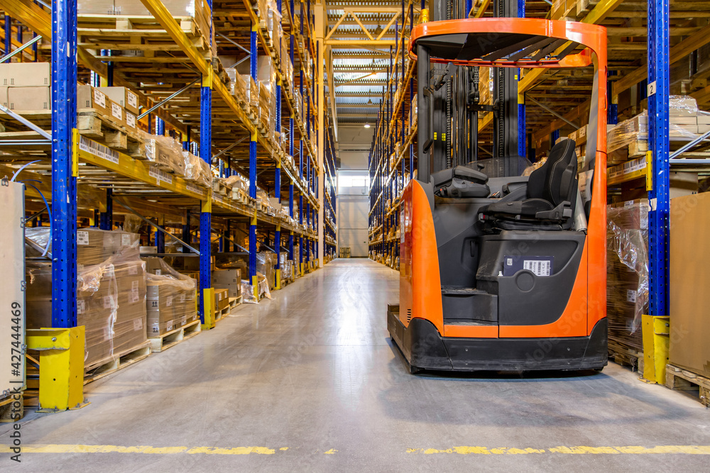 Interior of a modern warehouse storage with rows and goods boxes on high shelves. Pallet truck parking near shelves Interior of a modern warehouse storage with rows and goods boxes on high shelves. Pallet truck parking near shelves