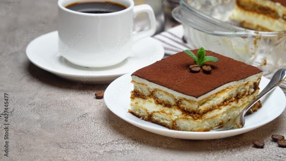 Traditional Italian Tiramisu dessert in glass baking dish and portion on grey concrete background Traditional Italian Tiramisu dessert in glass baking dish and portion on grey concrete background