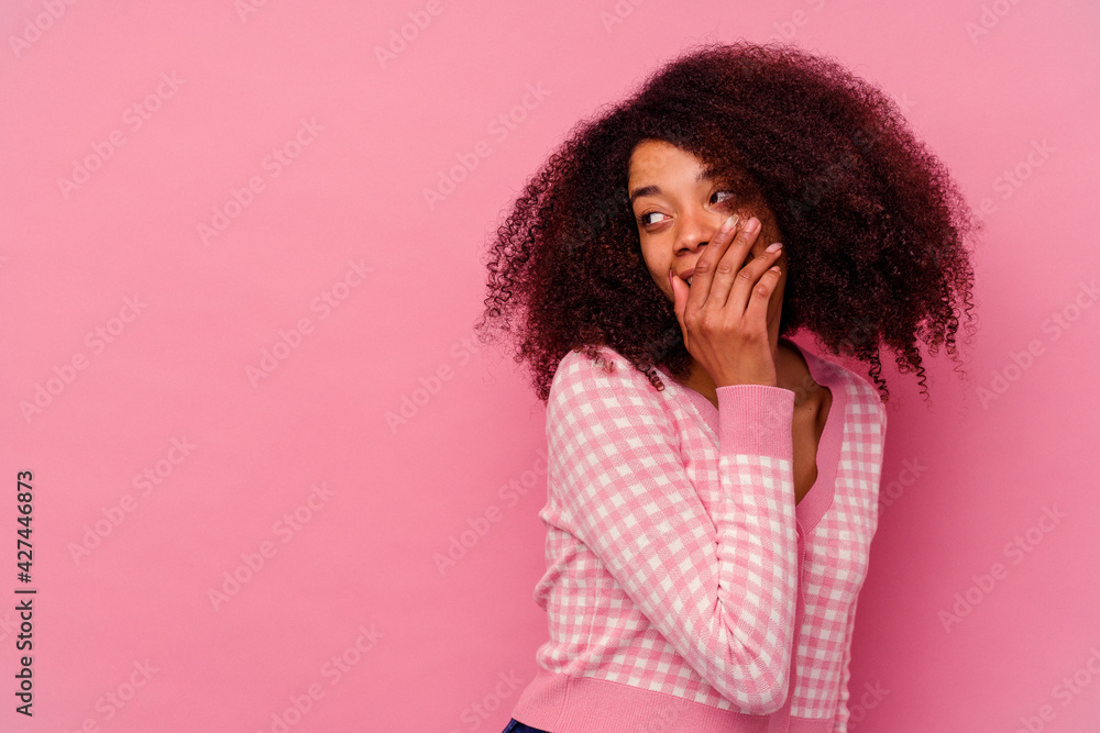 Young african american woman isolated on pink background thoughtful looking to a copy space covering mouth with hand. Young african american woman isolated on pink background thoughtful looking to a copy space covering mouth with hand.