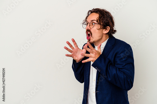 Young business man isolated on white background shouts loud, keeps eyes opened and hands tense.