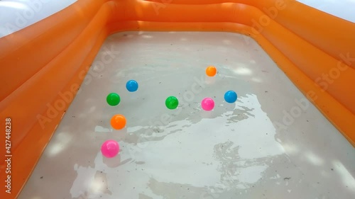 A basin of orange water with colorful balls waiting on the water surface.