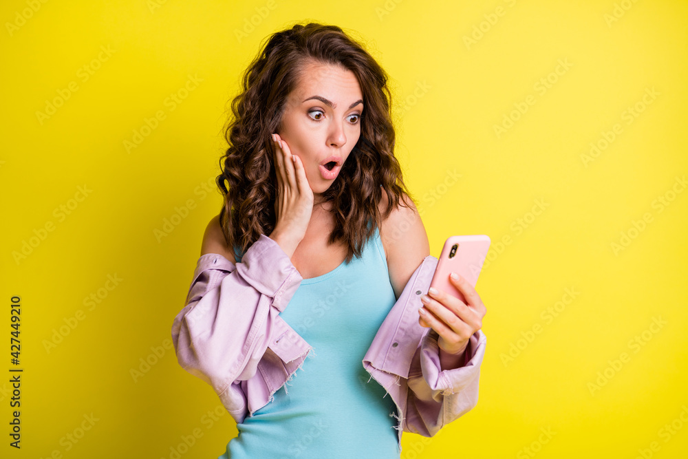 Portrait of attractive amazed wavy-haired girl using gadget browsing multimedia news isolated over bright yellow color background Portrait of attractive amazed wavy-haired girl using gadget browsing multimedia news isolated over bright yellow color background