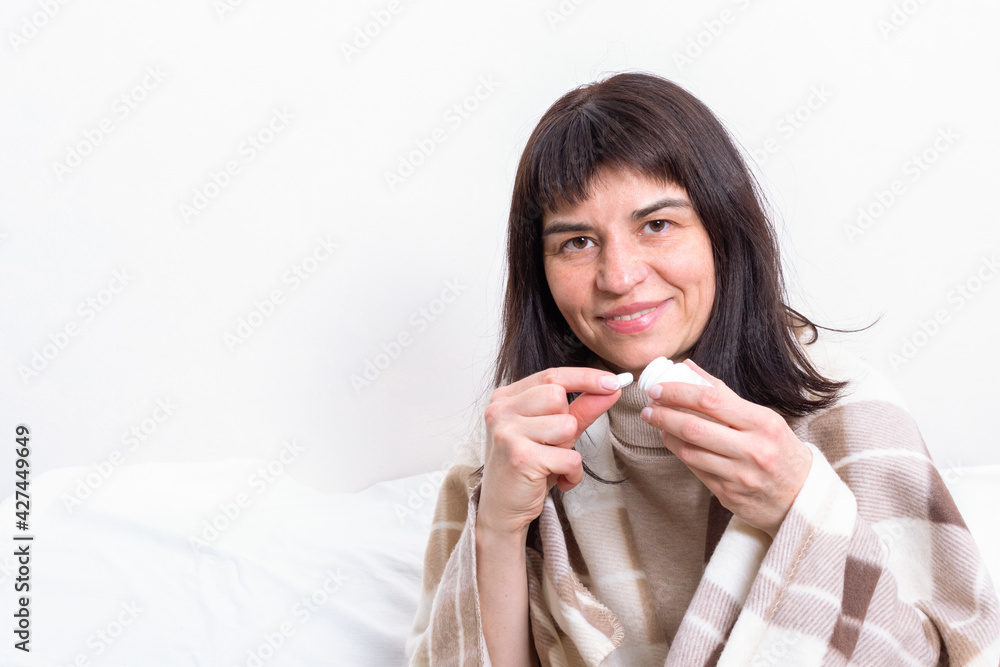 Young beautiful smiling woman covered with blanket holding vitamin pill while sitting on sofa at home. Young beautiful smiling woman covered with blanket holding vitamin pill while sitting on sofa at home.