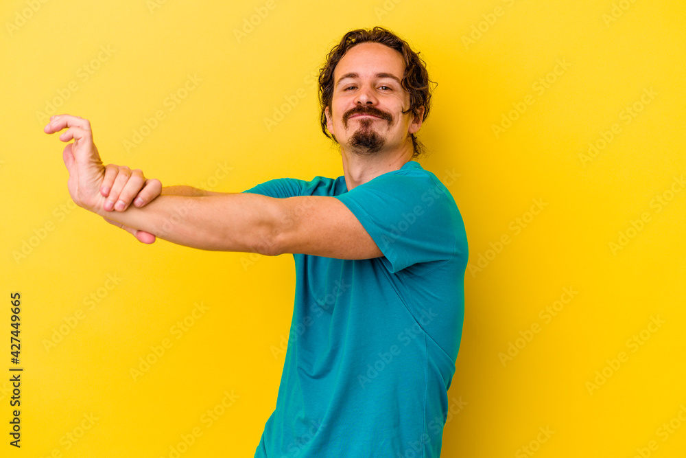 Young caucasian man isolated on yellow background stretching arms, relaxed position. Young caucasian man isolated on yellow background stretching arms, relaxed position.