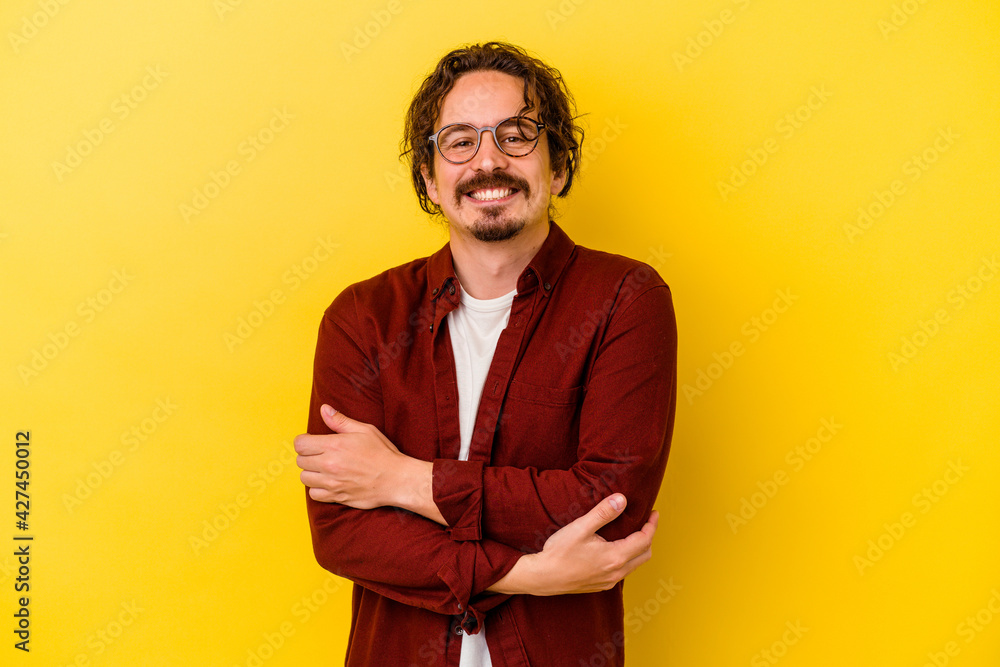 Young caucasian man isolated on yellow background who feels confident, crossing arms with determination.