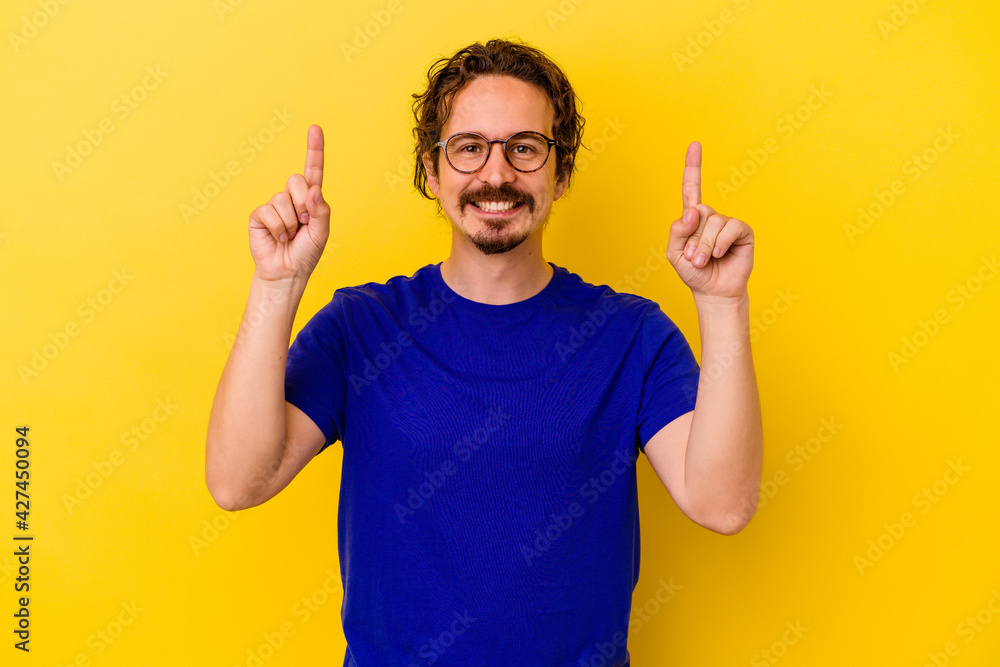 Young caucasian man isolated on yellow background indicates with both fore fingers up showing a blank space. Young caucasian man isolated on yellow background indicates with both fore fingers up showing a blank space.